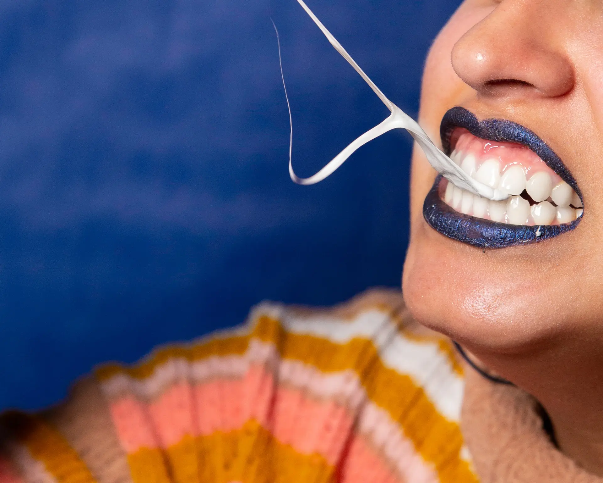 person with blue lips and white teeth pulling chewing gum from their mouth in strings - chewing gum dental health