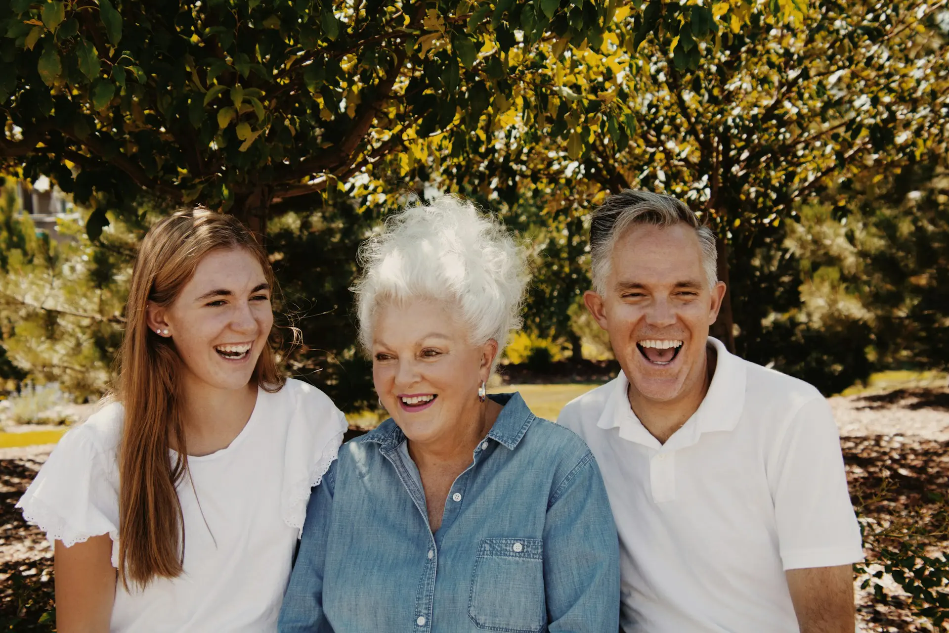young woman in white, older woman in blue, middle aged man in blue, with big smiles
