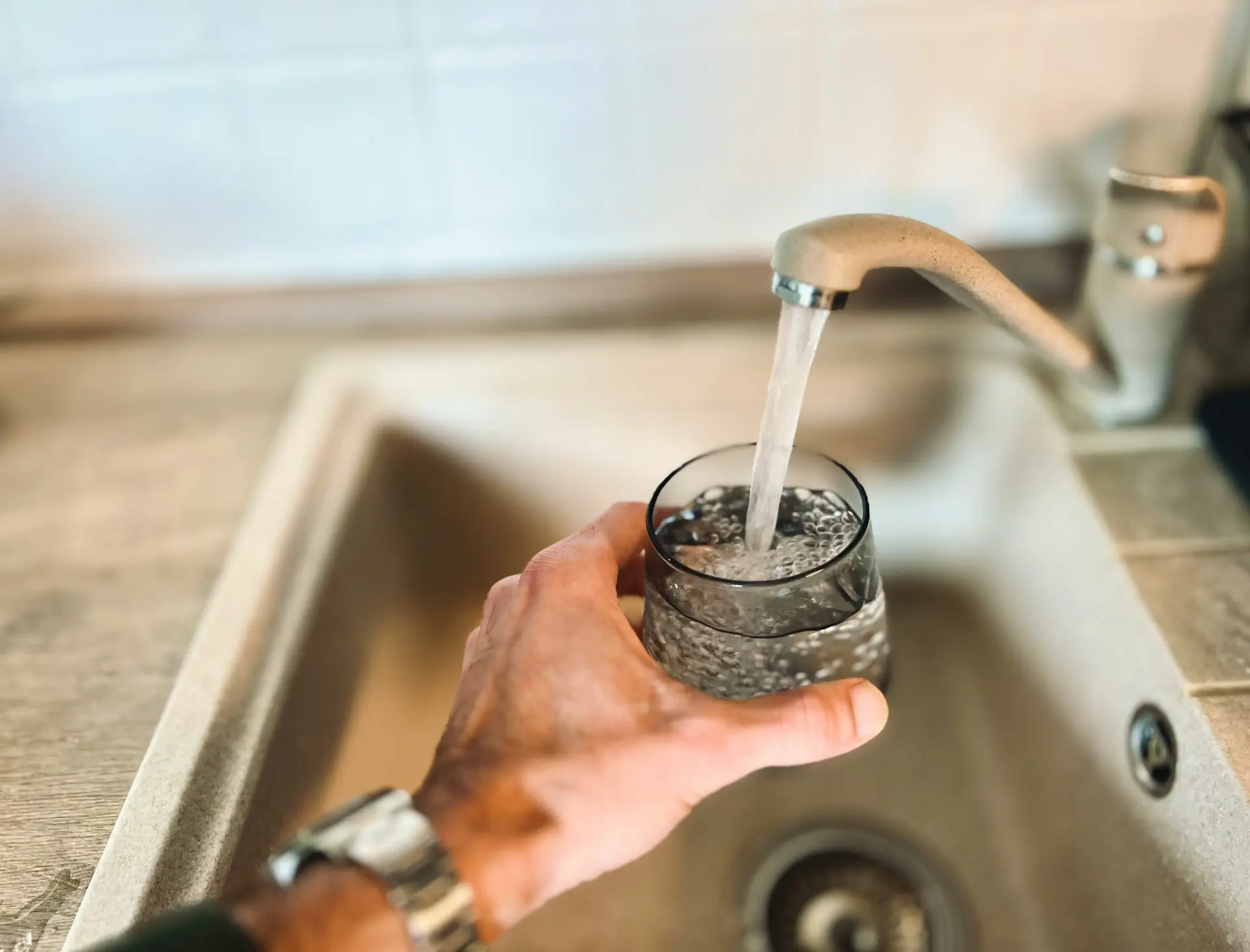 A male hand holding a glass and getting water from the kitchen faucet.
