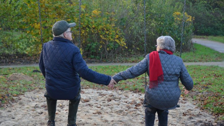 backs of two people holding hands outdoors