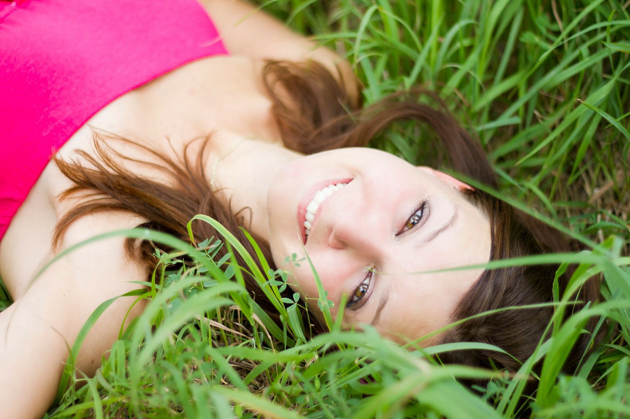 girl laying in grass smiling- what makes teeth yellow?