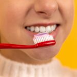 woman holding red toothbrush about to brush teeth - how to brush teeth