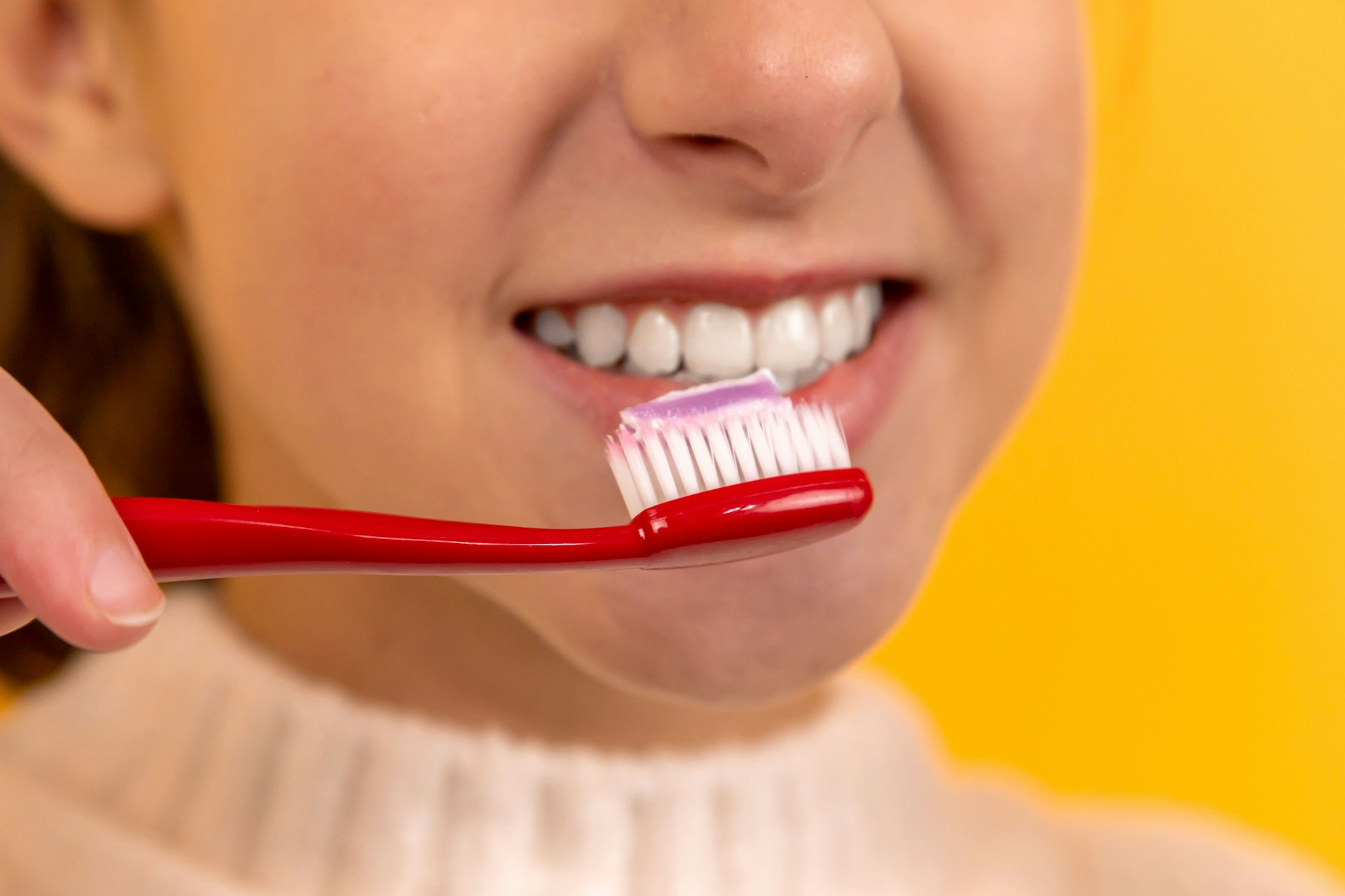 woman holding red toothbrush about to brush teeth - how to brush teeth