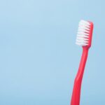 red toothbrush on a blue backdrop- how store a toothbrush